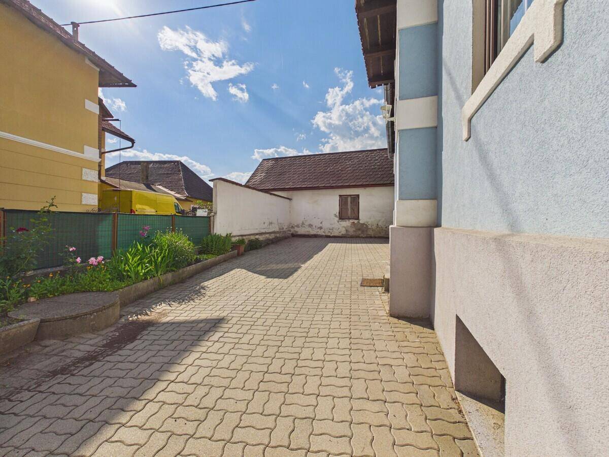 Gepflasterter Hofbereich neben dem Haus mit blauer Fassade und sonnigem Wetter.
