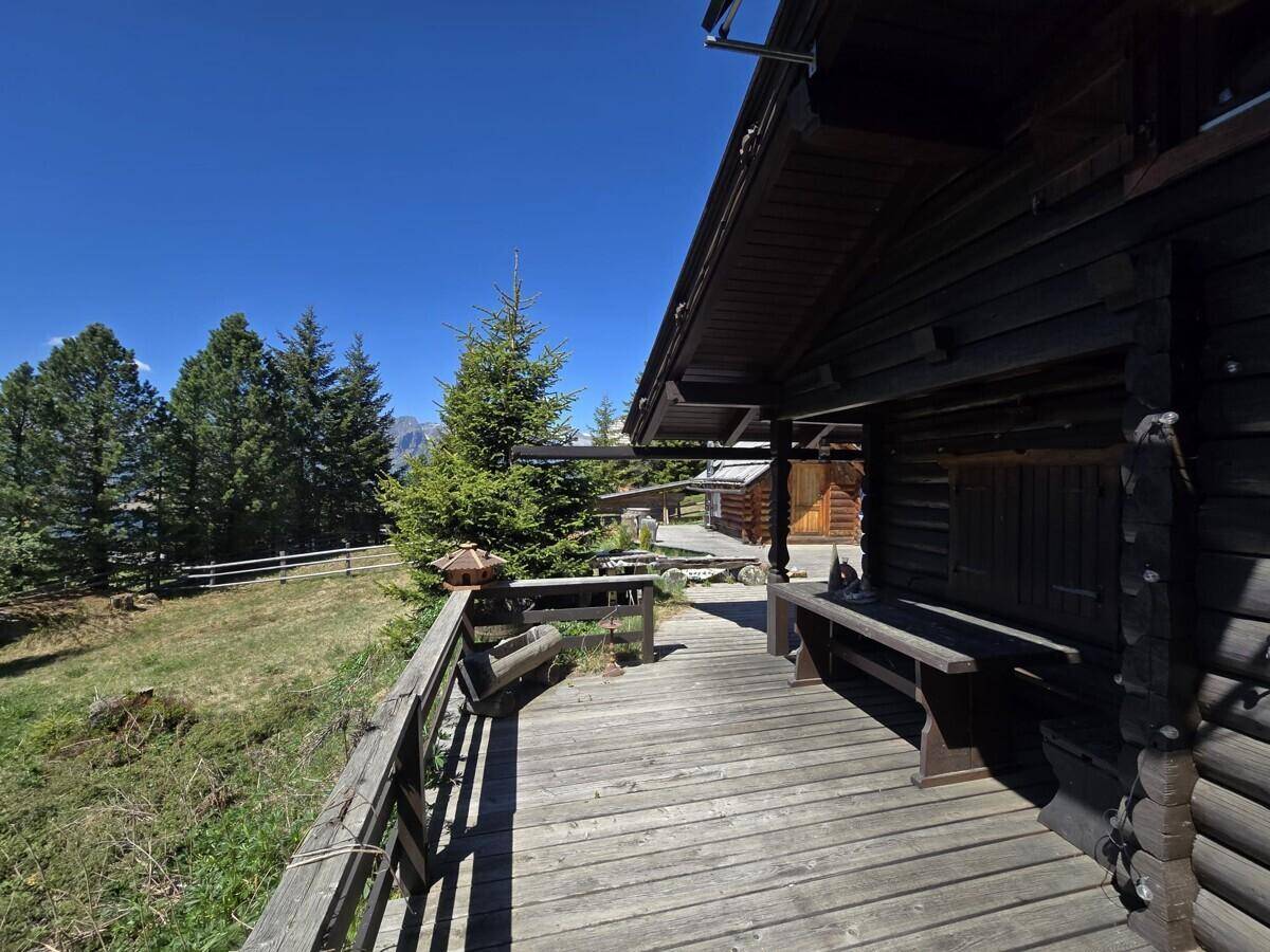 Holzterrasse entlang des Hauses mit rustikaler Bank und Blick auf die Natur.