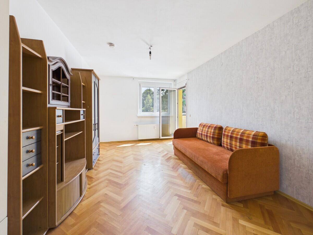 Geräumiges Wohnzimmer mit Fischgrätparkett, Sofa und Holzregalen, hell durch das Fenster.