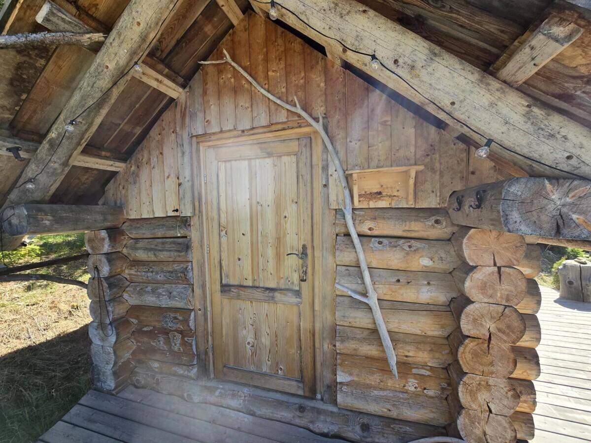 Rustikales Holzgebäude mit Holztür und Schindeldach, umgeben von einer Holzterrasse.