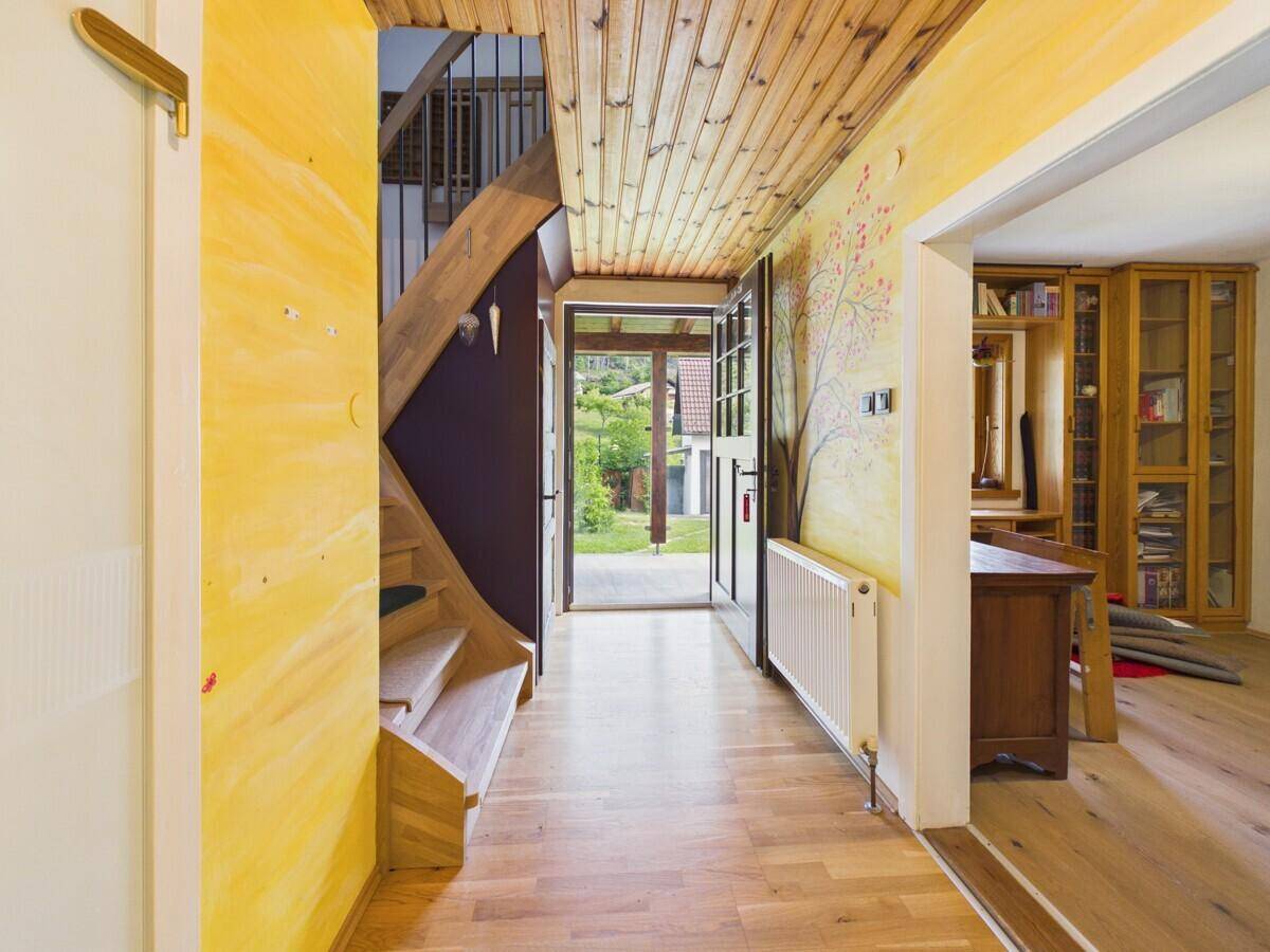 Heller Eingangsbereich mit gelb gestrichenen Wänden, Holzdecke und Treppe zum Obergeschoss.
