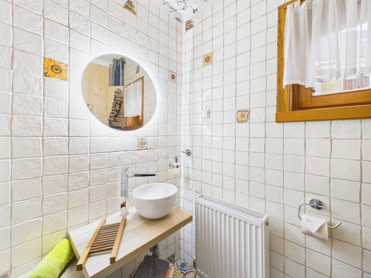 Badezimmer mit modernem Aufsatzwaschbecken, weiß gefliesten Wänden und Holzfensterrahmen.