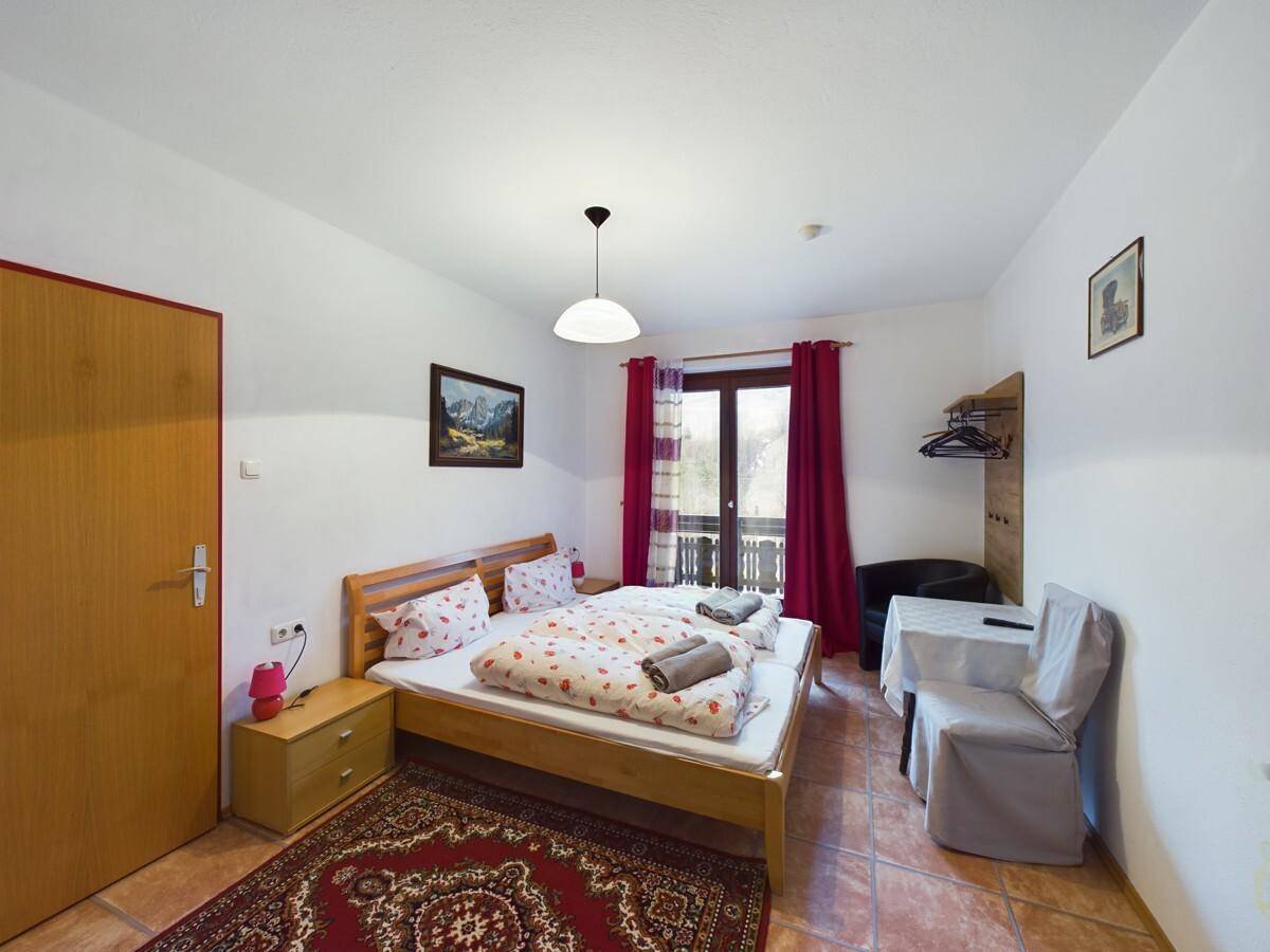 Schlafzimmer mit Doppelbett, Zugang zum Balkon und traditionellem Teppich auf Fliesenboden.