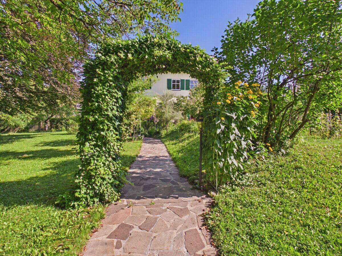 Idyllischer Gartenweg mit bewachsenem Torbogen, der zum Haus führt.