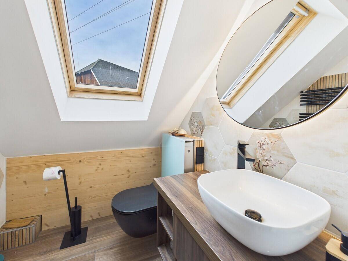 Helles Dachgeschoss-Badezimmer mit modernem Waschtisch, rundem Spiegel und Dachfenster.