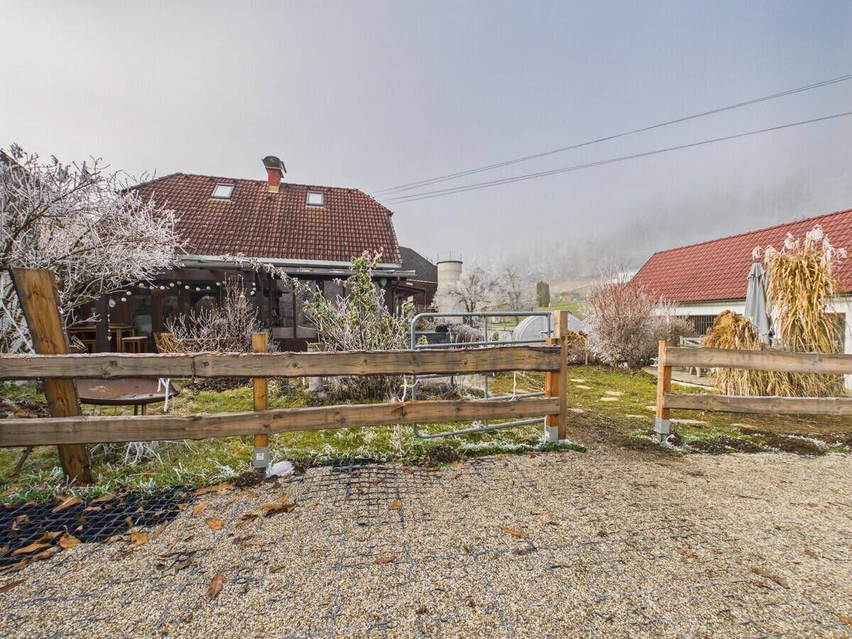 Ländliches Anwesen mit einem Wohnhaus, Holzzaun und einem Kiesweg im Vordergrund.