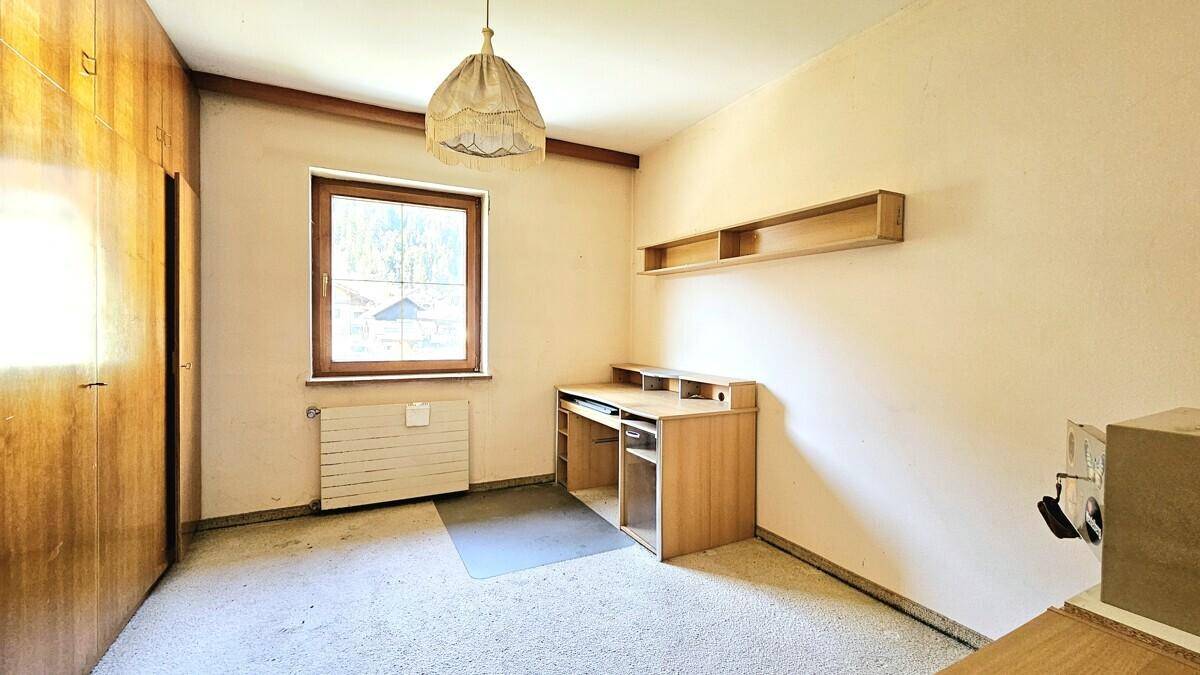Einfaches Schlafzimmer mit Teppichboden, Schreibtisch und Kleiderschrank.