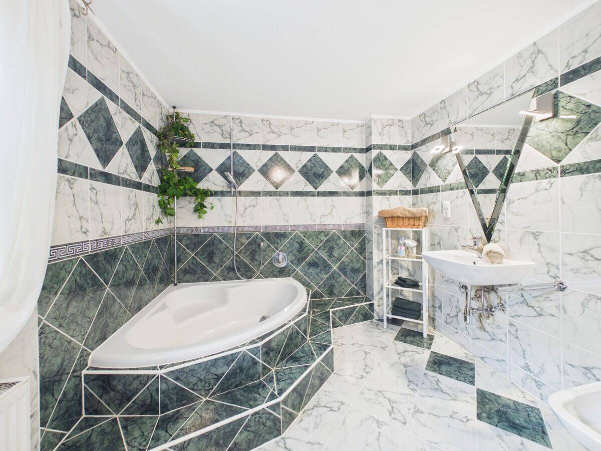 Geräumiges Badezimmer mit Eckbadewanne und auffälligen grün-weißen Marmorfliesen.