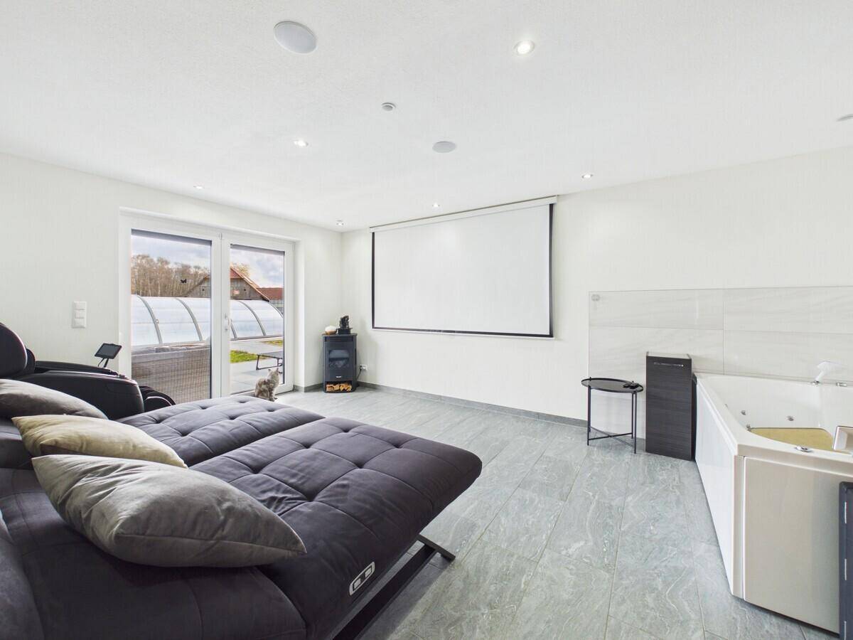 Unterhaltungsraum mit großem Sofa, Beamerleinwand und integriertem Whirlpool.