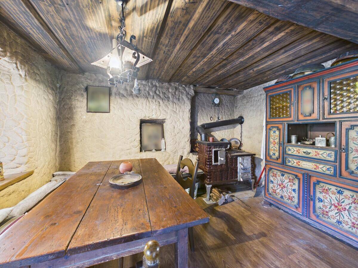 Rustikaler Essbereich mit Holztisch, traditionellem Ofen und bemalten Schränken.