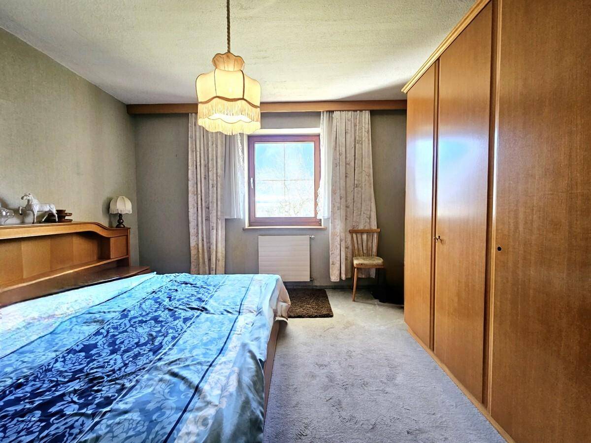 Schlafzimmer mit Teppichboden, Holzmöbeln und Fenster mit Blick ins Grüne.