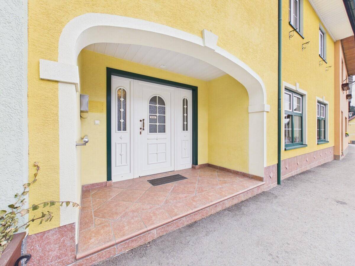 Traditioneller Hauseingang mit weißer Doppeltür, gelber Fassade und gefliestem Vordachbereich.
