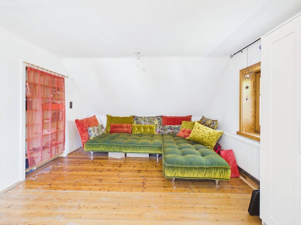 Helles Wohnzimmer mit schrägem Dach, Holzboden und einem großen grünen Samtsofa.