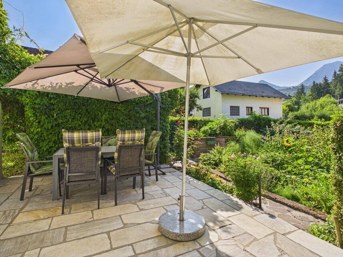 Gepflasterte Terrasse mit Gartenmöbeln und Sonnenschirmen, umgeben von Grün.