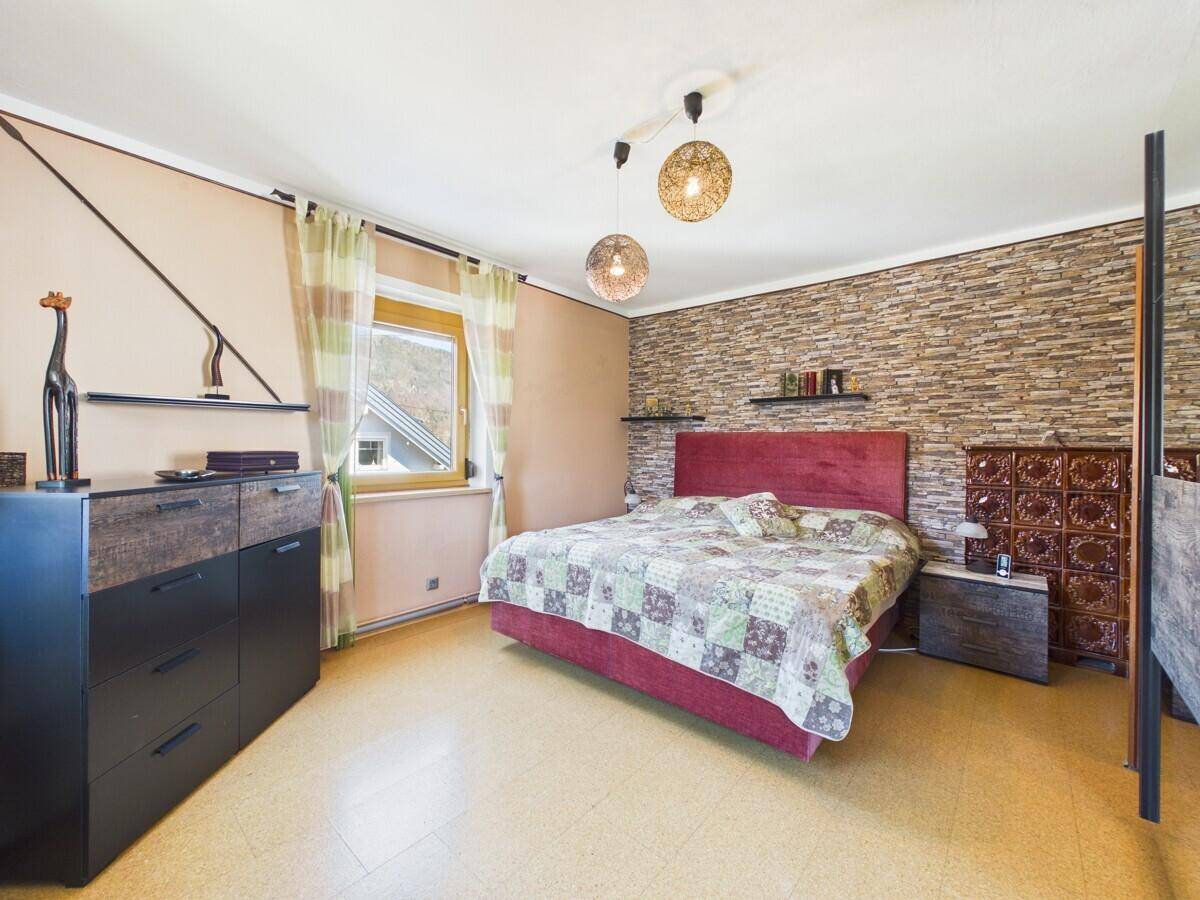 Gemütliches Schlafzimmer mit Doppelbett, Steinwandakzent und traditionellem Kachelofen.