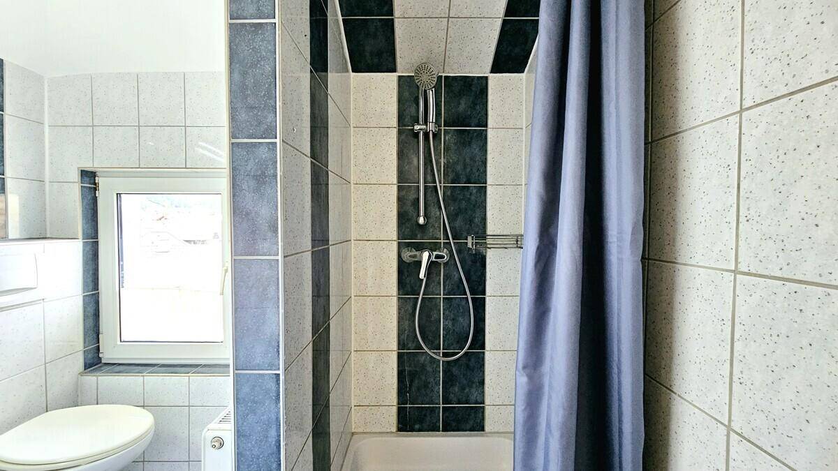 Duschbereich im Badezimmer mit Fliesen, Duschkopf und Fenster für Tageslicht.