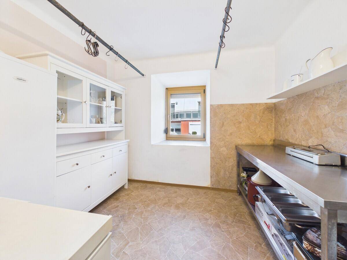 Funktionale Küche mit Edelstahl-Arbeitsflächen, weißem Schrank und Fenster für Tageslicht.