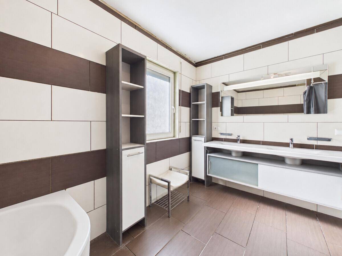 Geräumiges Badezimmer mit braun-weißen Fliesen, Doppelwaschbecken und Eckbadewanne.