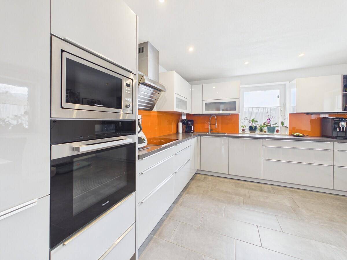 Moderne Küche mit weißen Hochglanzfronten, integrierten Geräten und orangefarbener Rückwand.