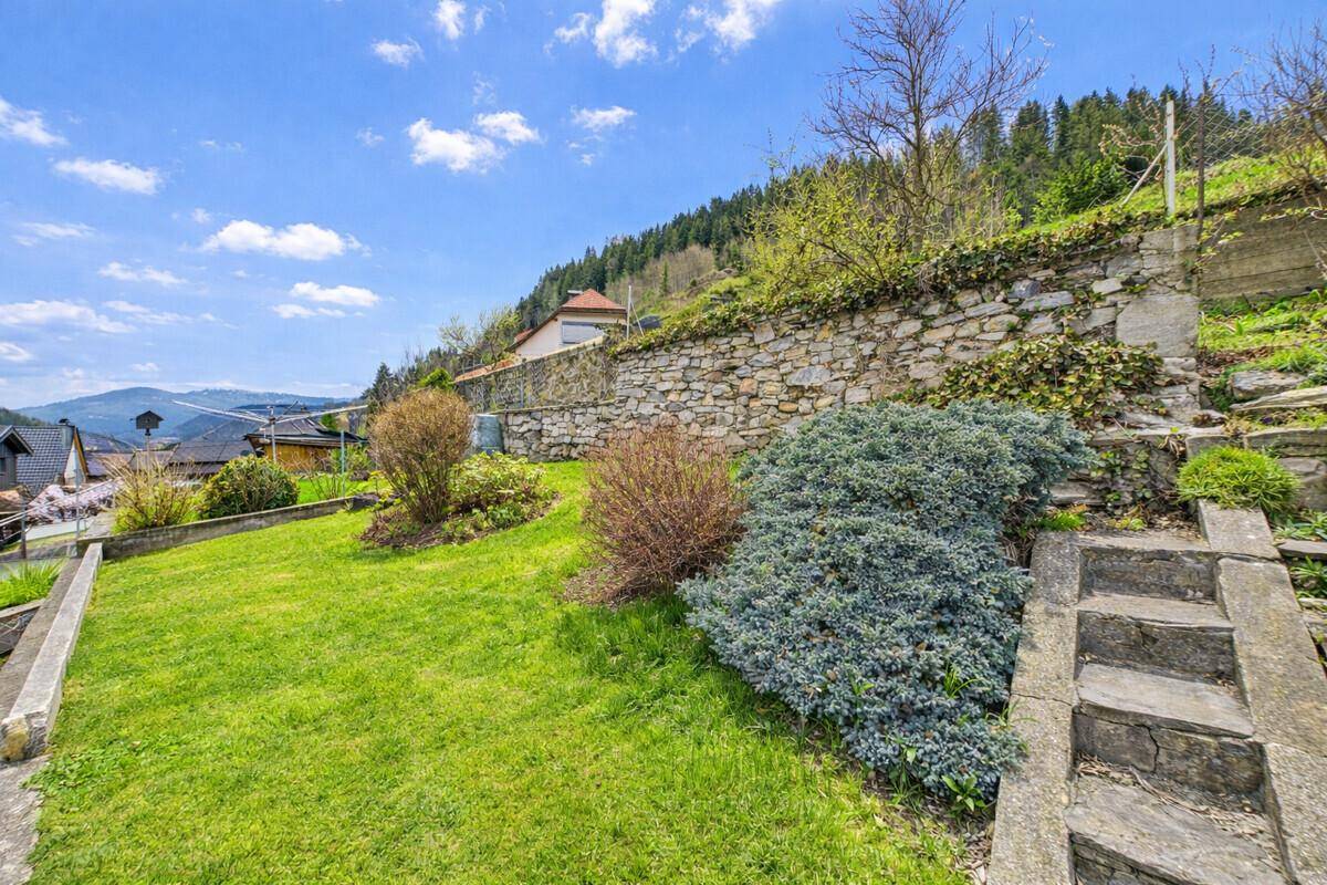Terrassierter Gartenbereich mit Rasenflächen, Sträuchern und einer Steinmauer im Hintergrund.