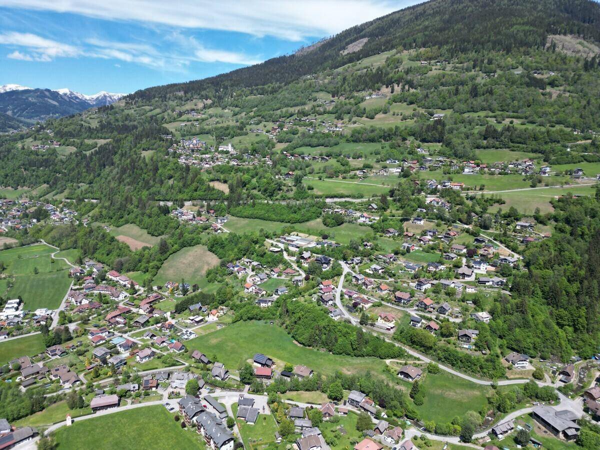 Weitläufige Luftaufnahme eines Dorfes in einem Tal mit schneebedeckten Bergen im Hintergrund.