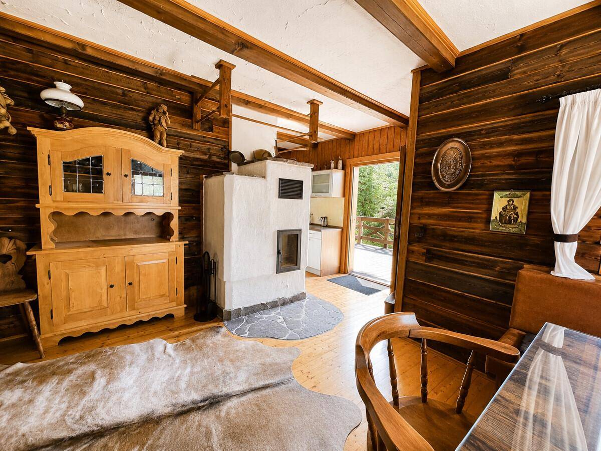 Rustikales Wohnzimmer mit Kachelofen, Holzbalken und traditionellen Holzmöbeln, mit Zugang zur Terrasse.