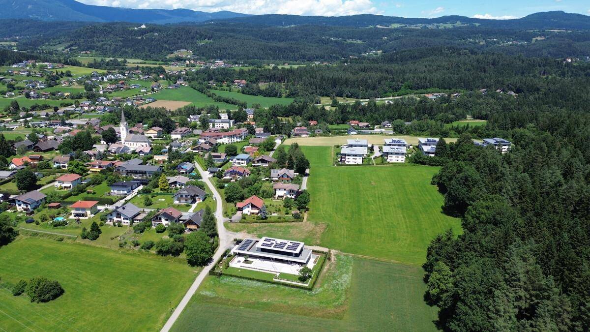 Luftaufnahme einer ländlichen Gegend mit einem modernen Gebäude im Vordergrund, umgeben von Feldern und Wäldern.