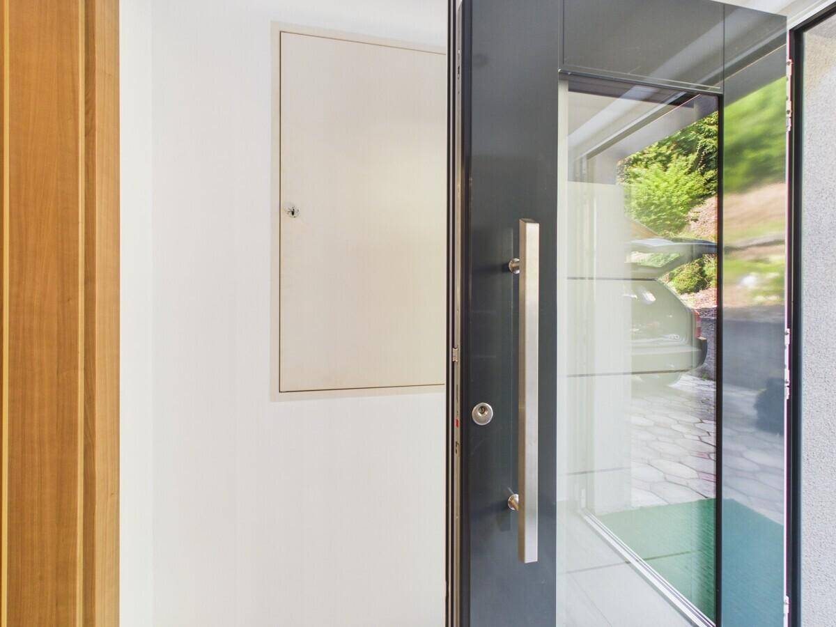 Moderne Eingangstür mit Glaseinsatz und elegantem Griff, die einen hellen Flur öffnet.