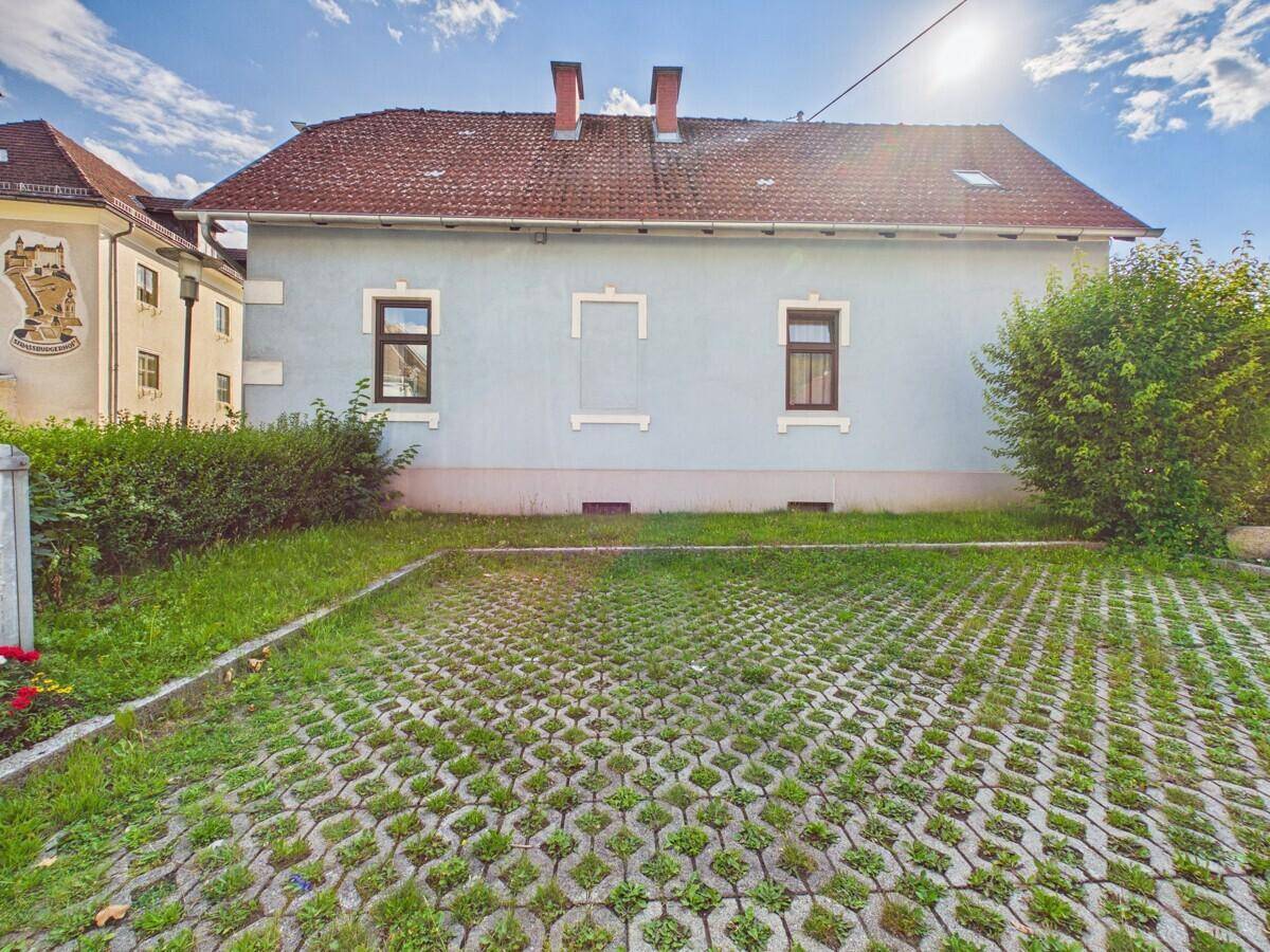 Rückseite des Hauses mit begrüntem Parkplatz und einer Hecke.