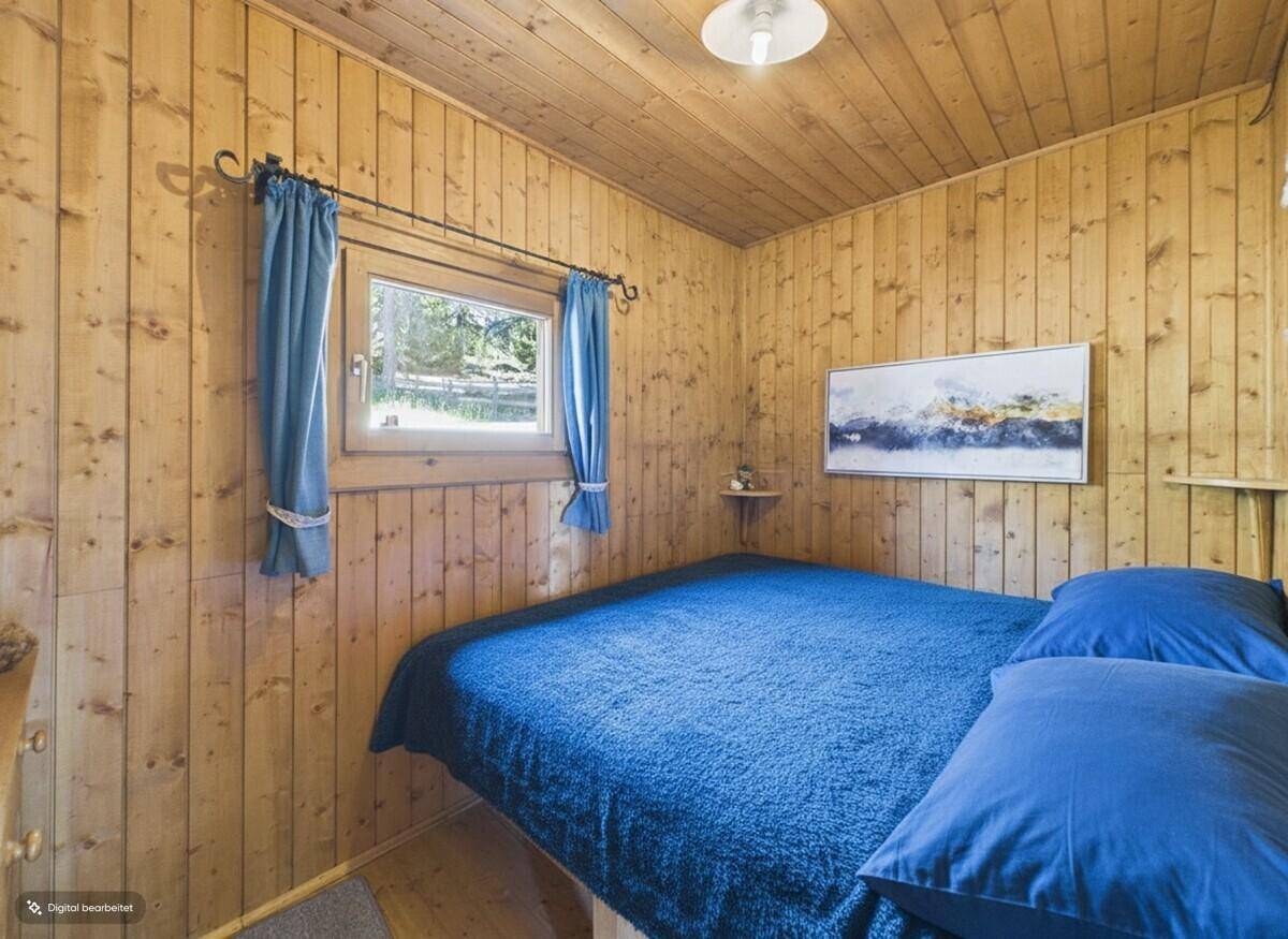 Schlafzimmer mit Holzwänden, blauem Bett und Vorhängen, bietet eine ruhige Atmosphäre.