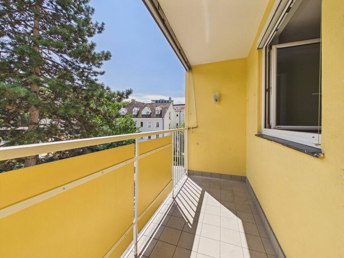 Heller Balkon mit gelben Wänden, Fliesenboden und Blick auf die umliegenden Dächer.
