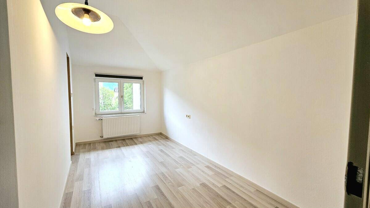 Helles Schlafzimmer mit Dachschräge, Laminatboden und Fenster mit Ausblick.