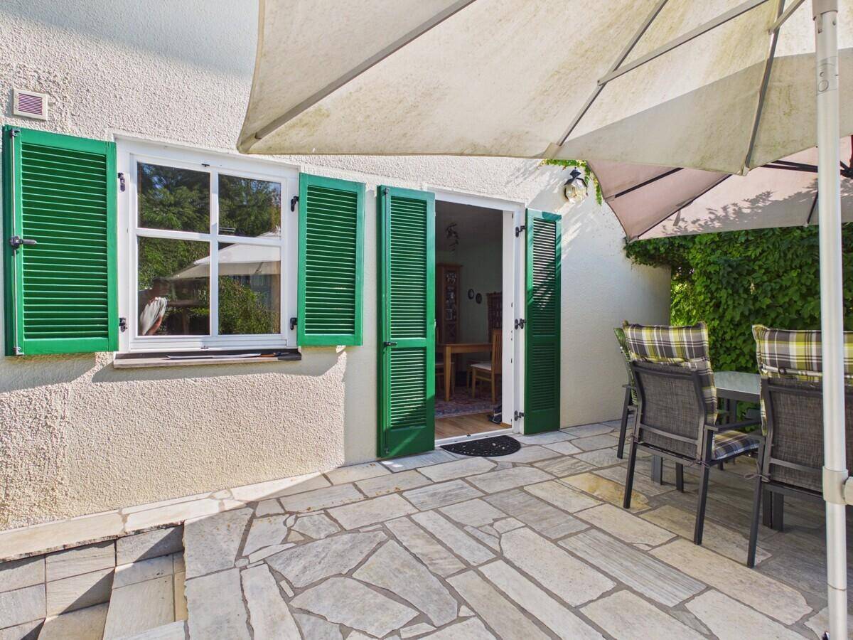 Gemütlicher Sitzbereich auf der Steinterrasse mit Sonnenschirm und grünen Fensterläden.