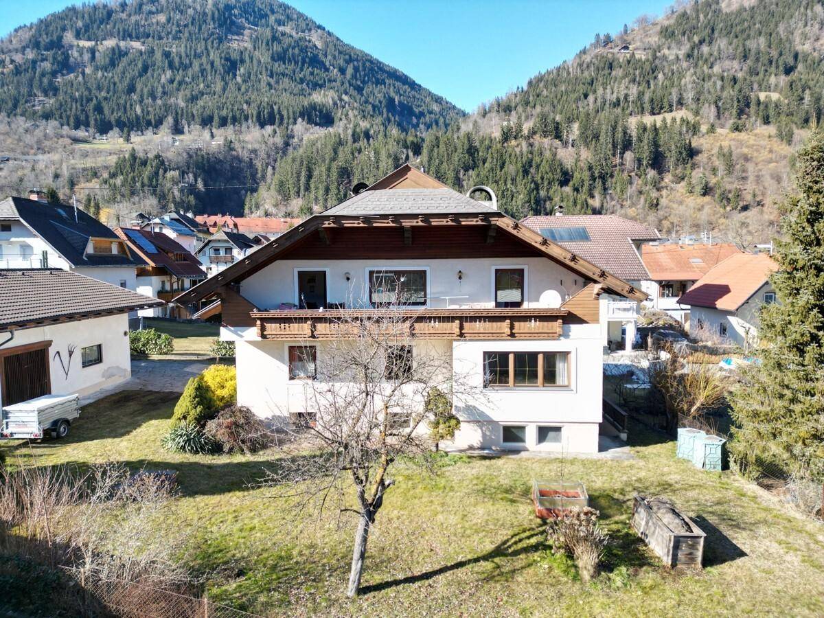 Hausfassade mit Holzbalkonen und Garten, umgeben von einer malerischen Berglandschaft.