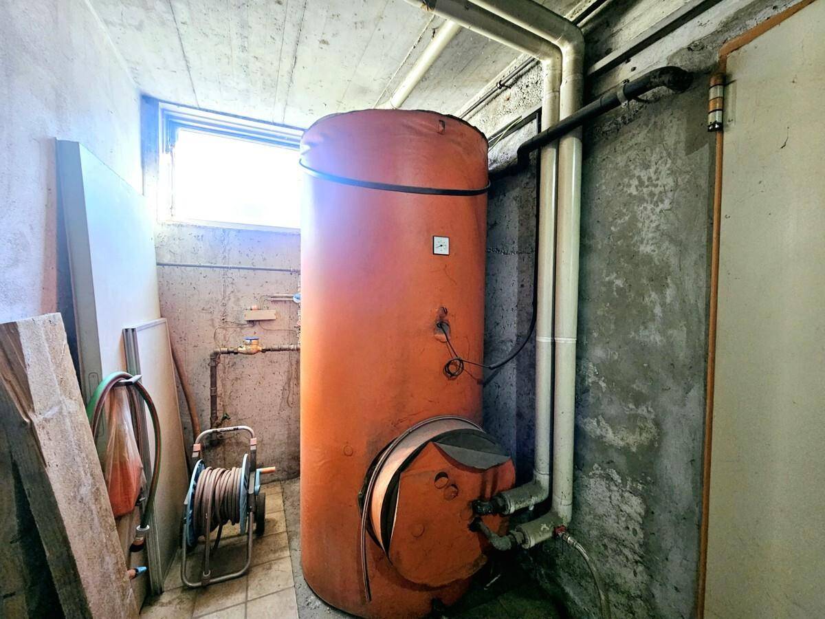 Heizungsraum im Keller mit großem Warmwasserspeicher und Rohren.