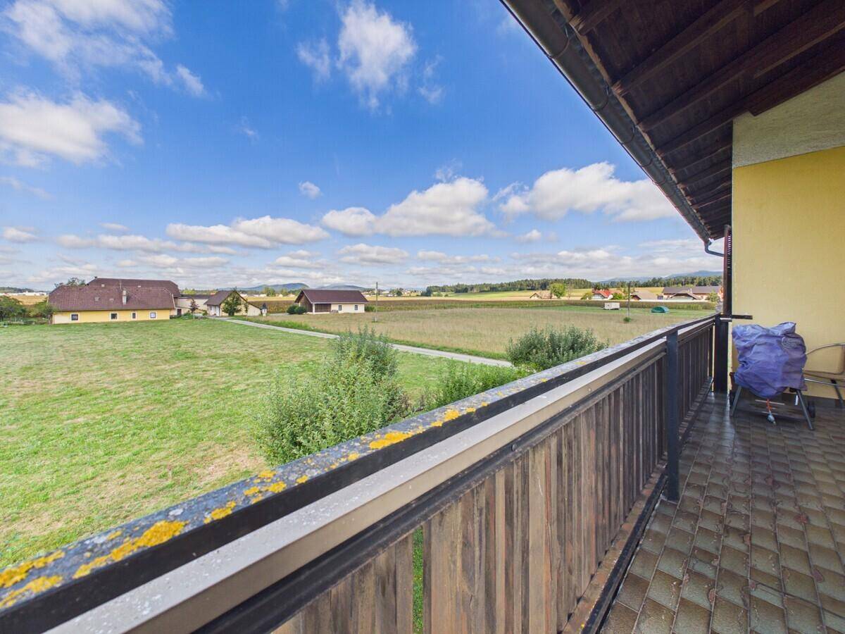 Balkon mit gefliestem Boden und Holzgeländer, mit Blick auf Felder und Häuser.