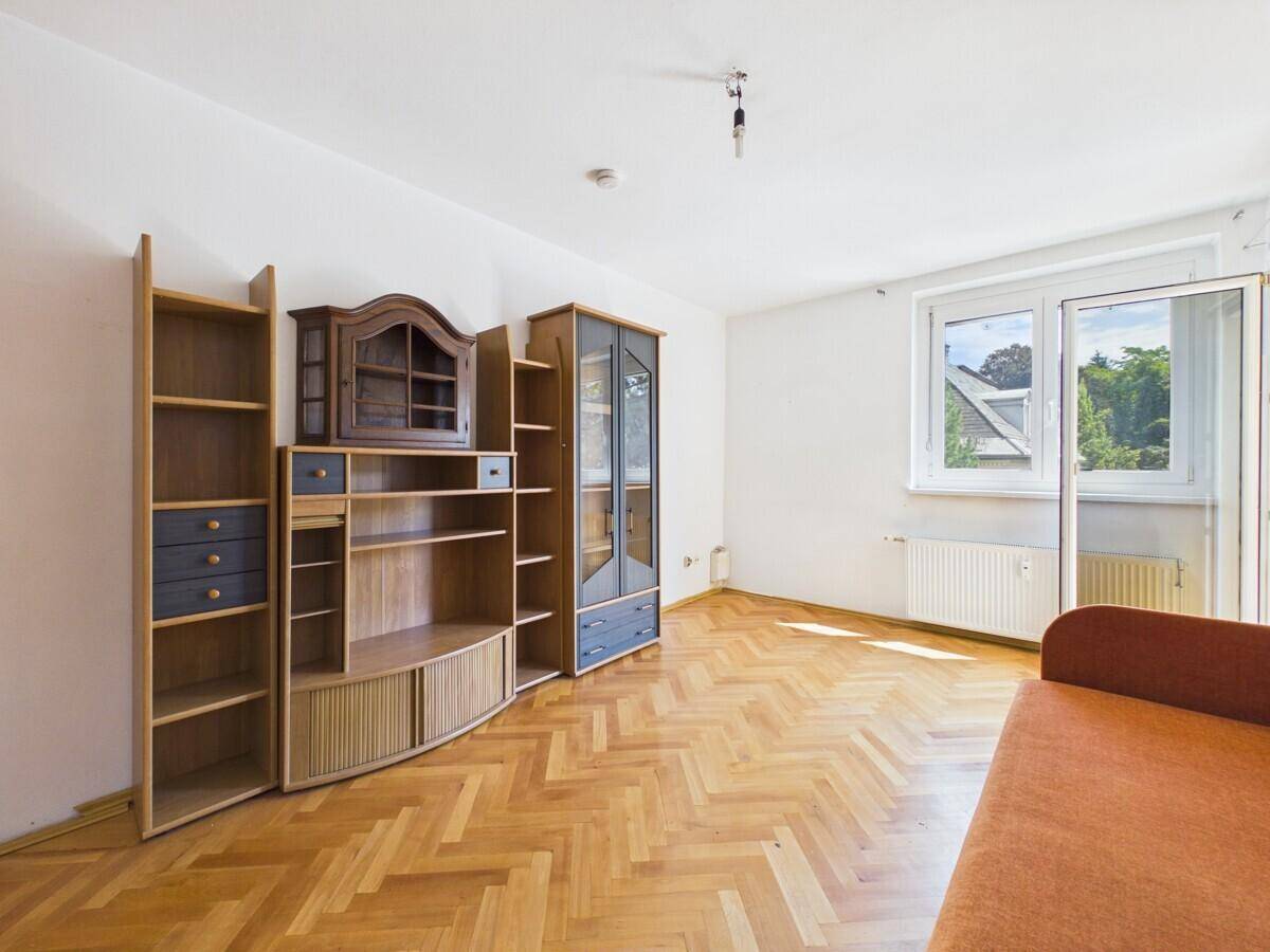 Geräumiges Wohnzimmer mit Fischgrätparkett, Sofa und Holzmöbeln, hell durch Fenster.
