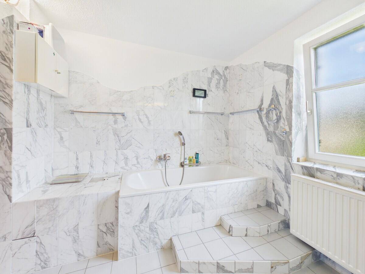 Helles Badezimmer mit Badewanne, Marmorfliesen und Fenster für Tageslicht.