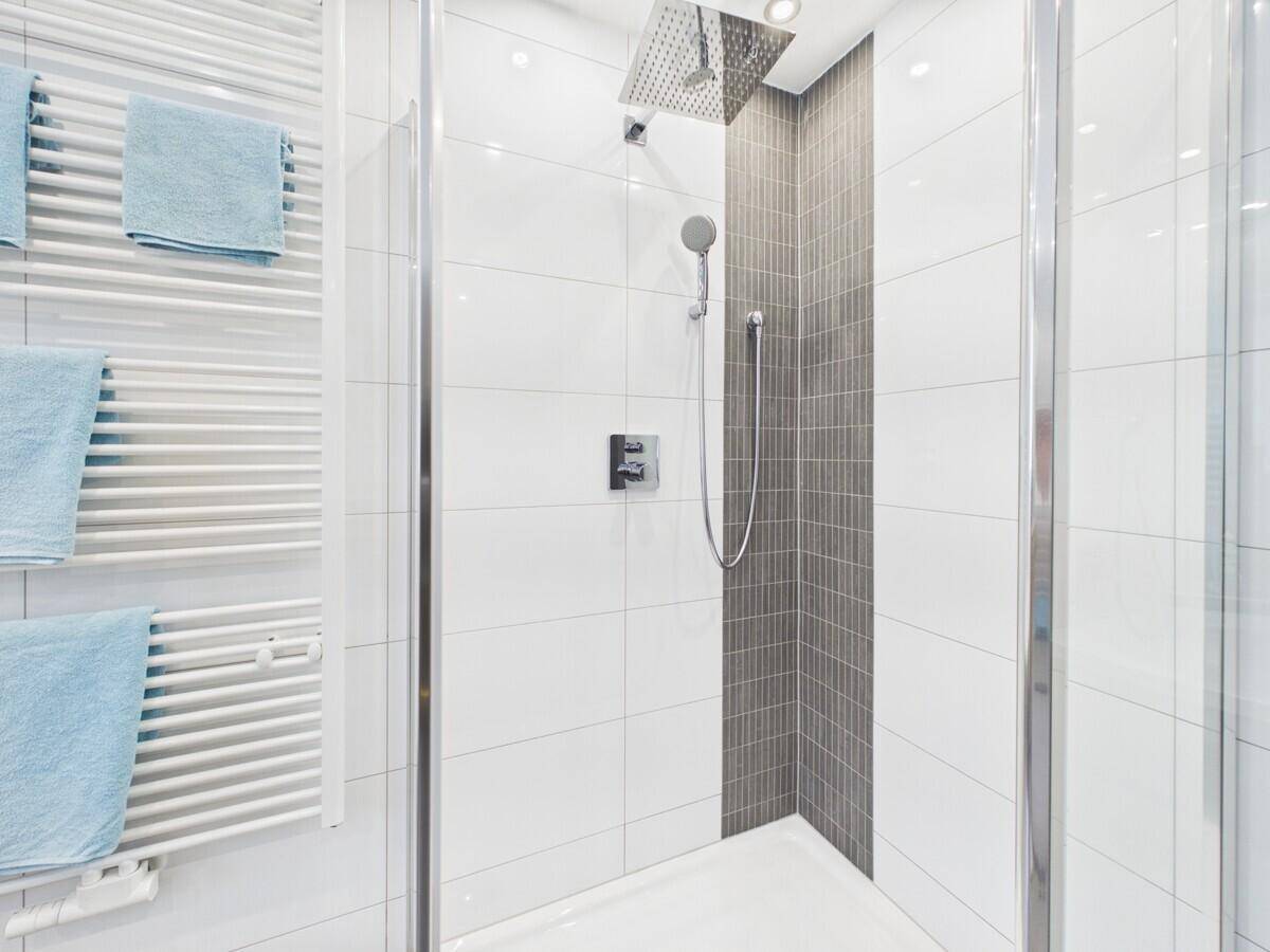 Moderne Duschkabine mit Regendusche und Handbrause, umgeben von weißen und grauen Fliesen.