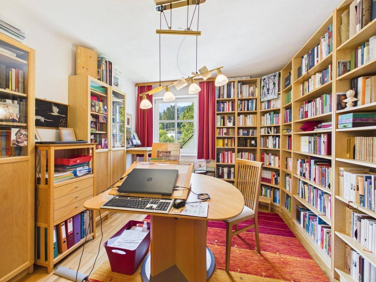 Großes Arbeitszimmer mit umfangreichen Bücherregalen, Schreibtisch und Blick ins Grüne.