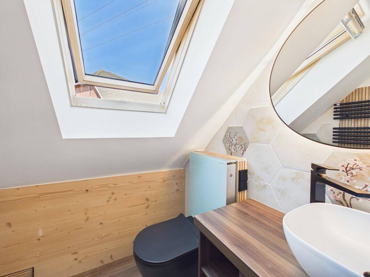 Dachgeschoss-Badezimmer mit modernem WC, Holzwaschtisch und großem Dachfenster.