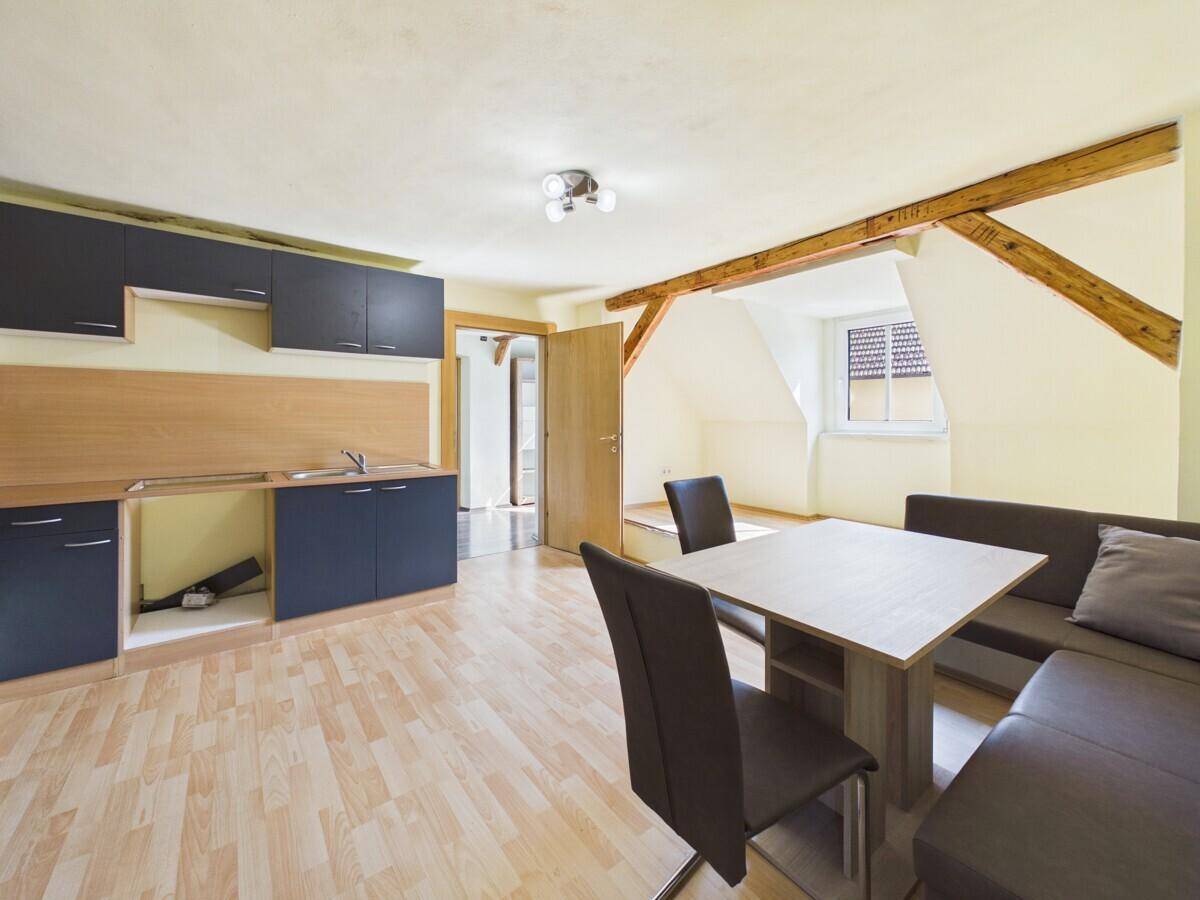Offener Wohnbereich im Dachgeschoss mit Küchenzeile und Essbereich, unter sichtbaren Holzbalken.