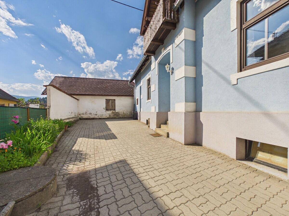 Gepflasterte Einfahrt neben einem hellblauen Haus unter blauem Himmel.