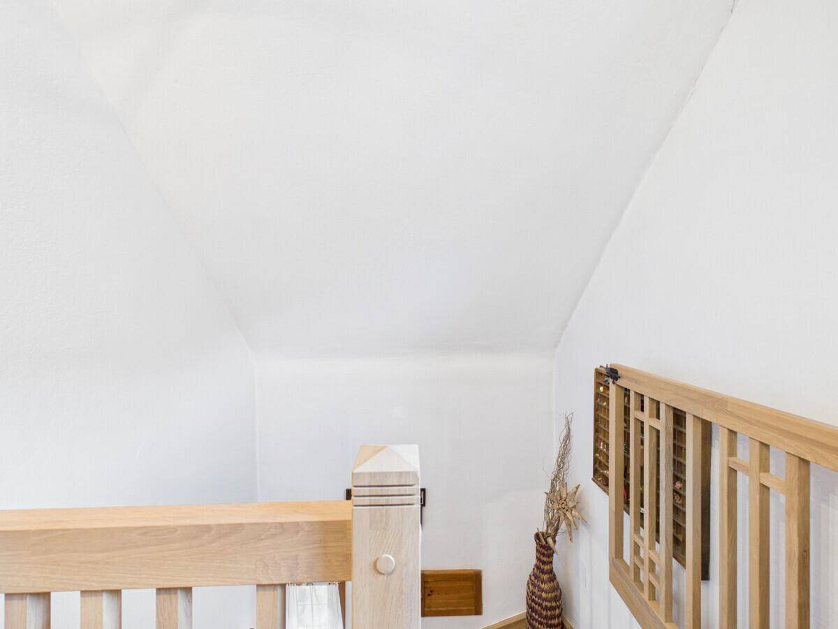 Heller Treppenabsatz im Dachgeschoss mit Holzgeländer und schrägen Wänden.