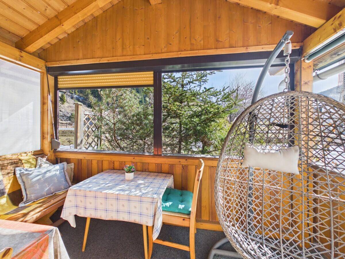 Gemütliche überdachte Loggia mit Esstisch und Hängesessel, umgeben von Natur und Bergblick.
