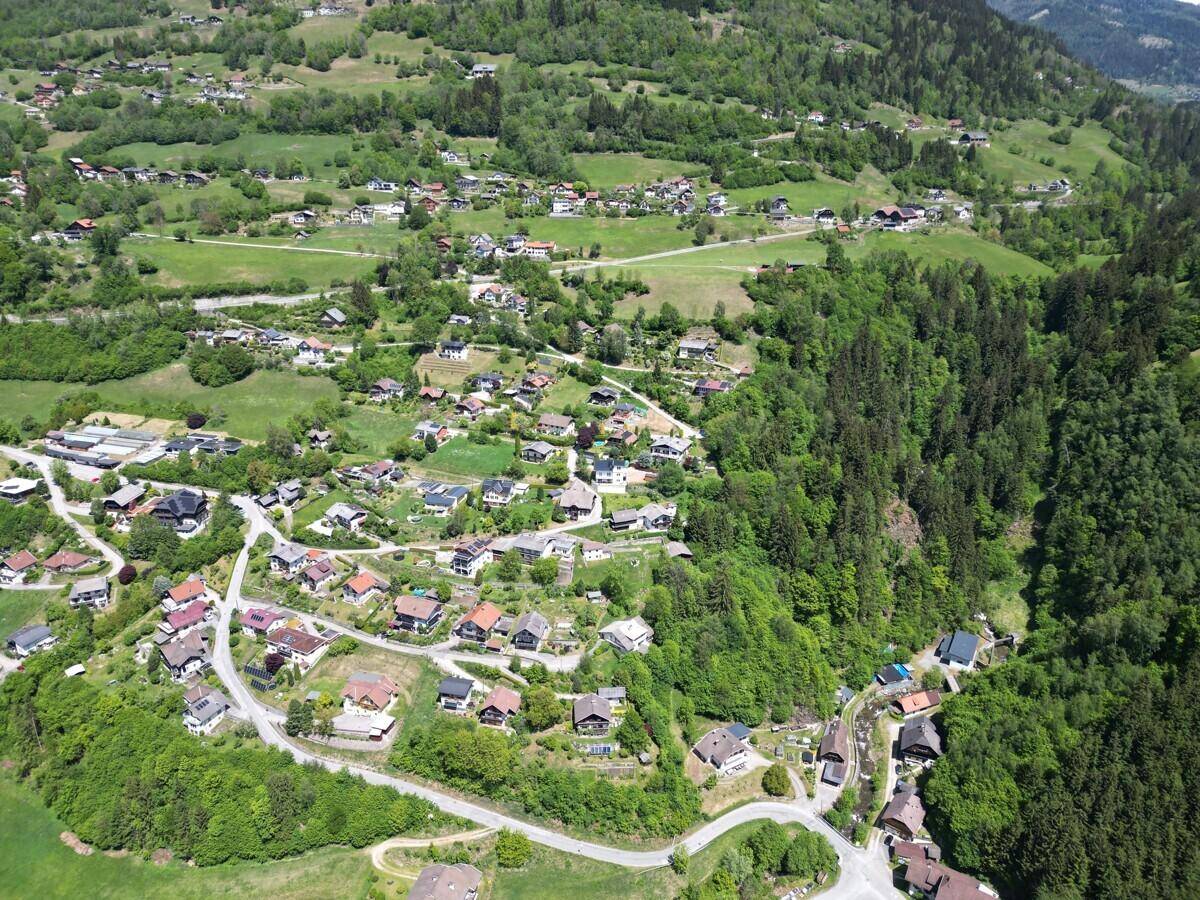 Luftaufnahme eines malerischen Dorfes, eingebettet in eine grüne Hügellandschaft mit vielen Bäumen.