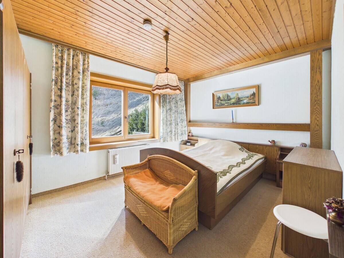 Helles Schlafzimmer mit Holzdecke, Teppichboden und traditionellen Möbeln.