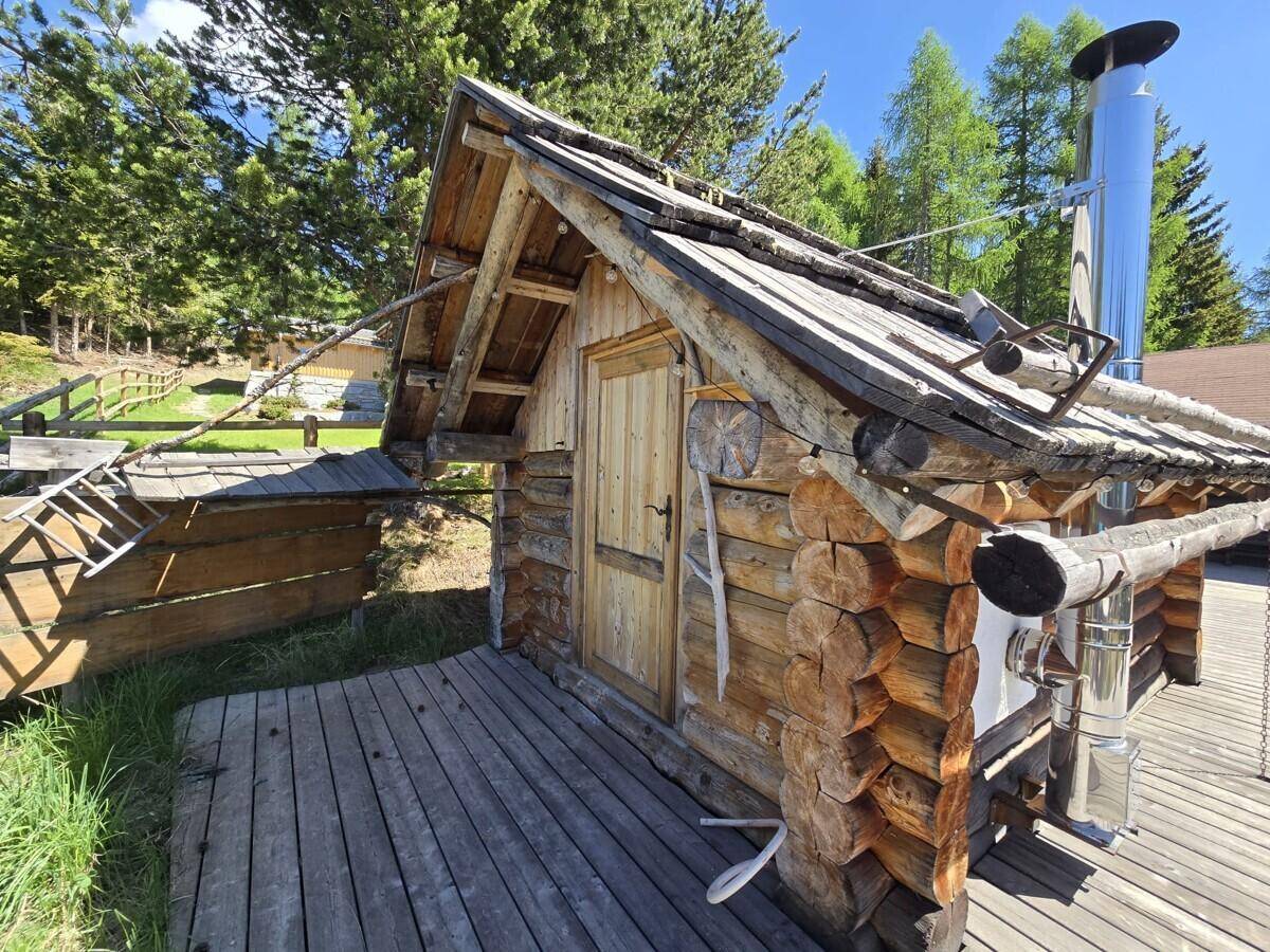 Rustikales Holzgebäude mit Schindeldach und Edelstahlkamin, umgeben von einer Holzterrasse.
