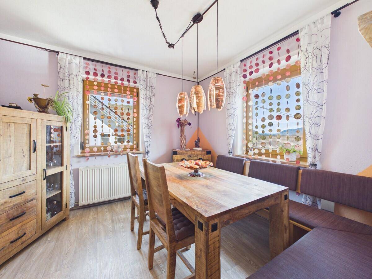 Gemütlicher Essbereich mit Holztisch, Eckbank und dekorativen Fenstervorhängen.