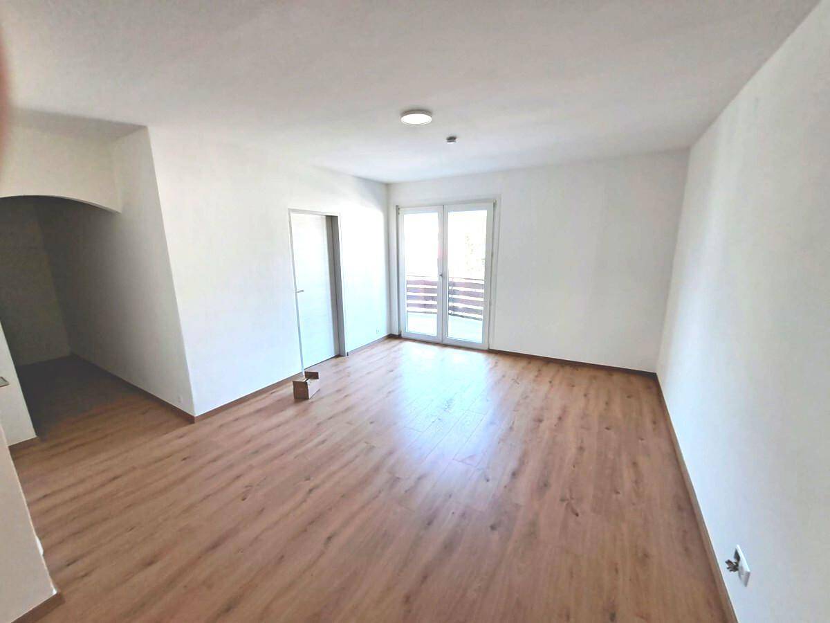 Geräumiges Zimmer mit Laminatboden, weißen Wänden und Zugang zu einem Außenbereich durch Doppeltüren.